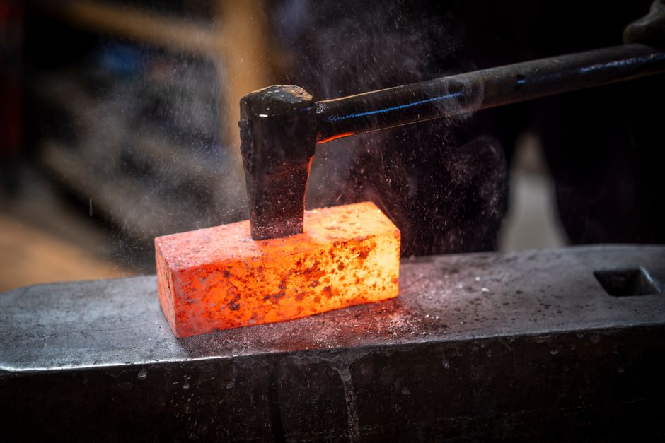 Blacksmith using a hammer to forge a glowing hot metal piece on an anvil. Industrial craftsmanship.